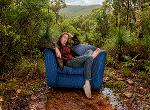 Me, draped over a blue sofa armchair placed in the middle of the Australian bush. The image is aggressively dithered.